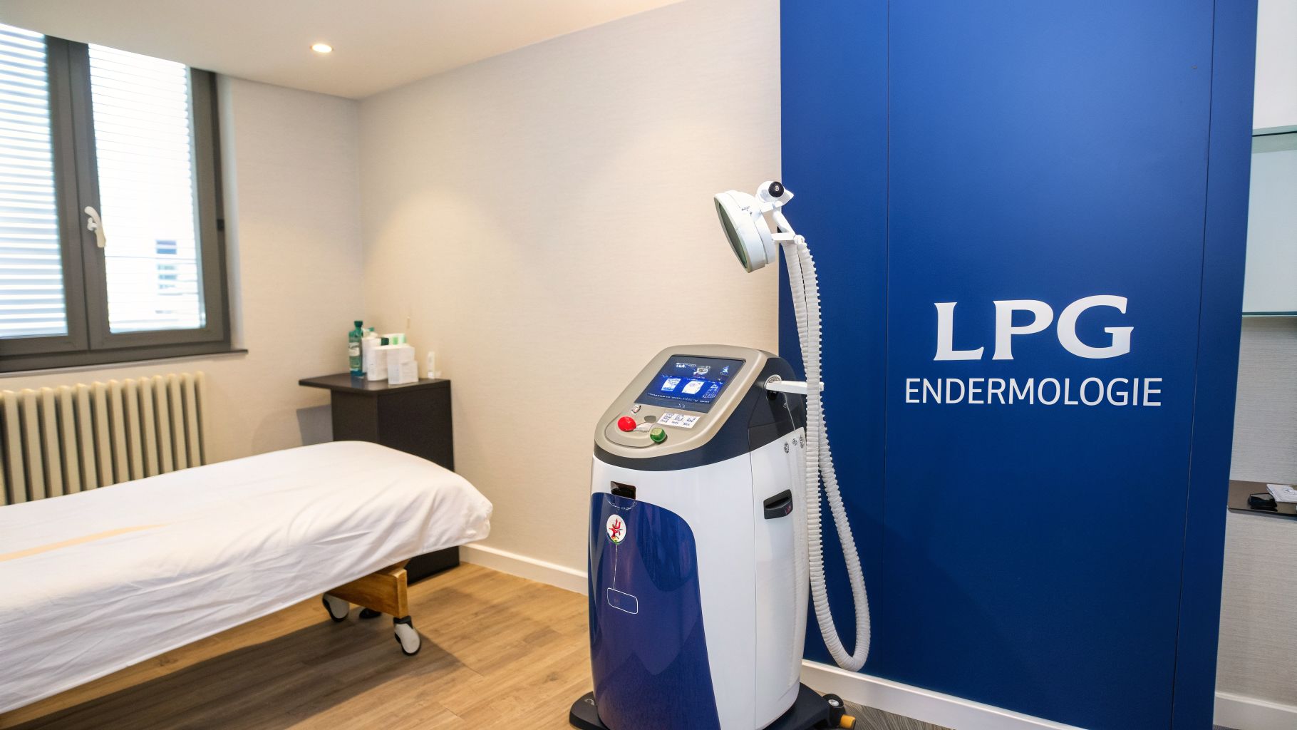 A clean treatment room featuring an LPG Endermologie machine, a comfortable bed, and a window with blinds.