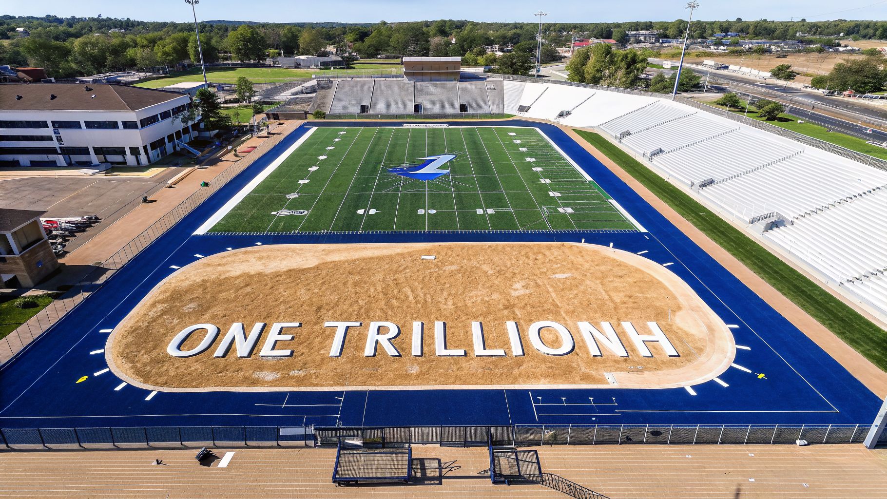 Aerial view of a football stadium with blue track, a sandy area, and 'ONE TRILLIONH' text.